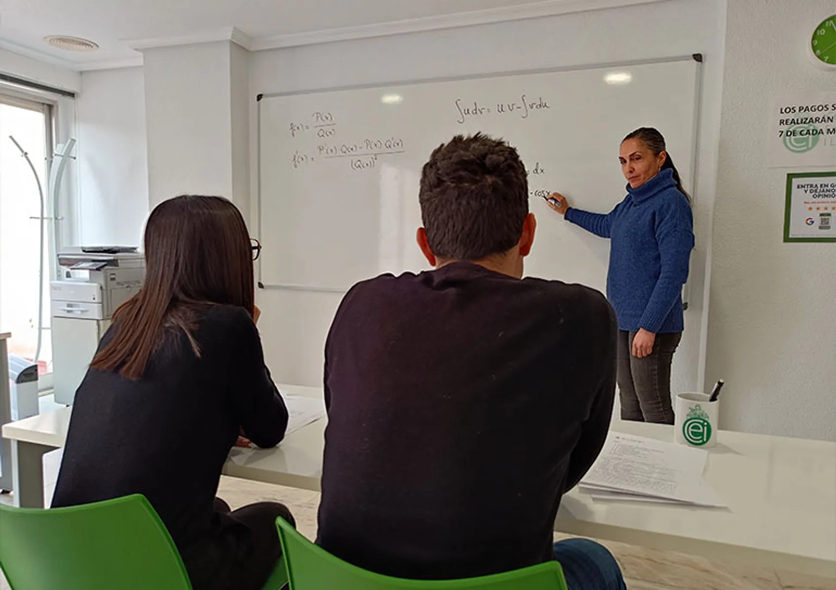 Una profesora explica en la pizarra a dos alumnos